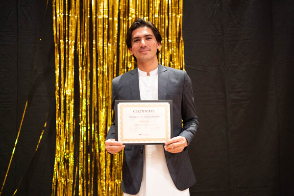 Student Abdul Aziz stands with a congratulatory certificate in hand. 
