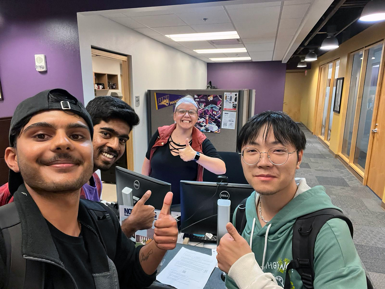 Three male international students and one female giving thumbs up.