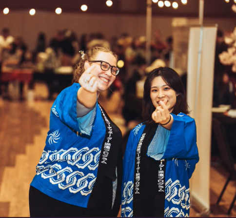 Image shows two women wearing traditional Japanese gear and posing with the camera with Finger Hearts